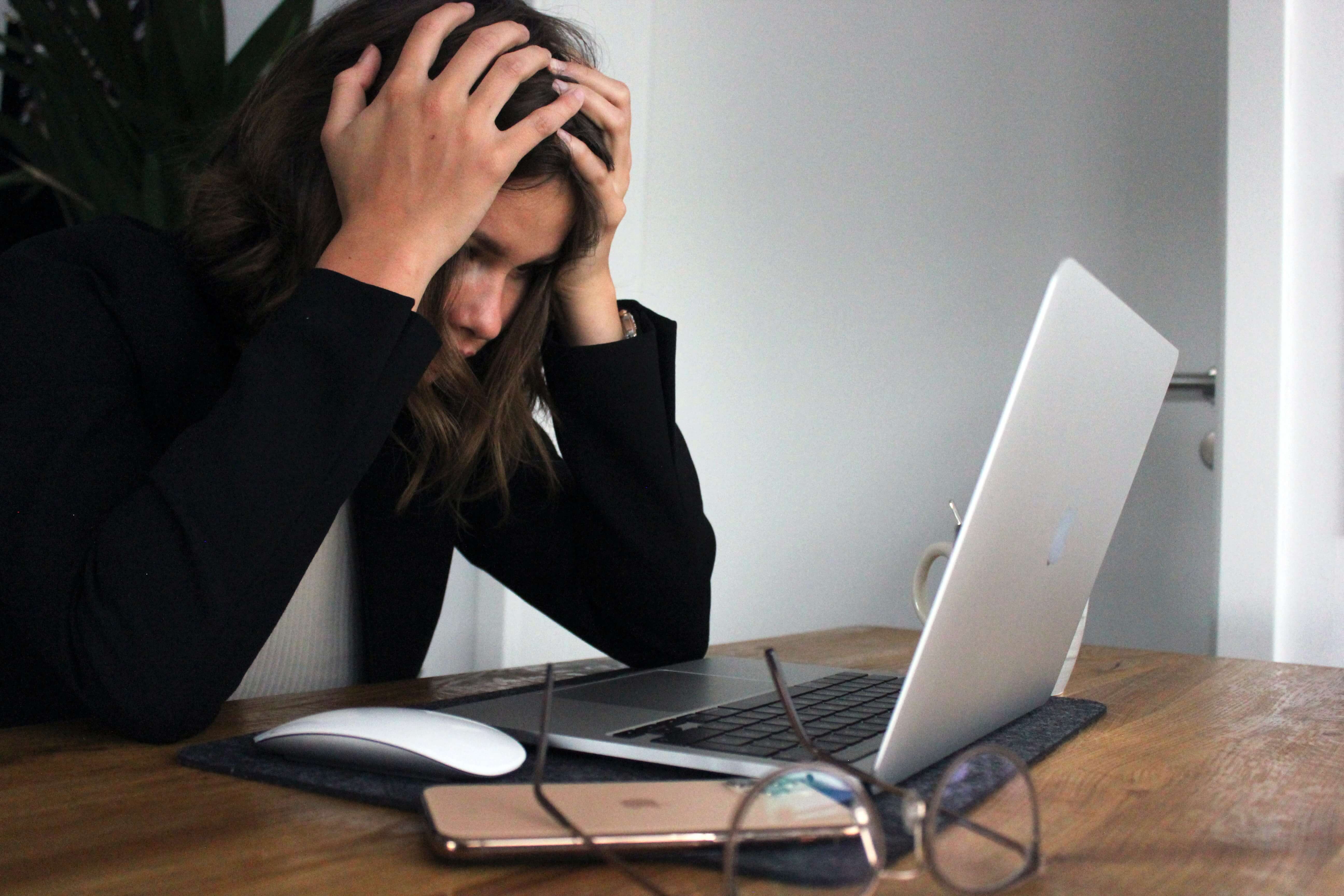 A woman grabbing her head in stress while looking at her computer.