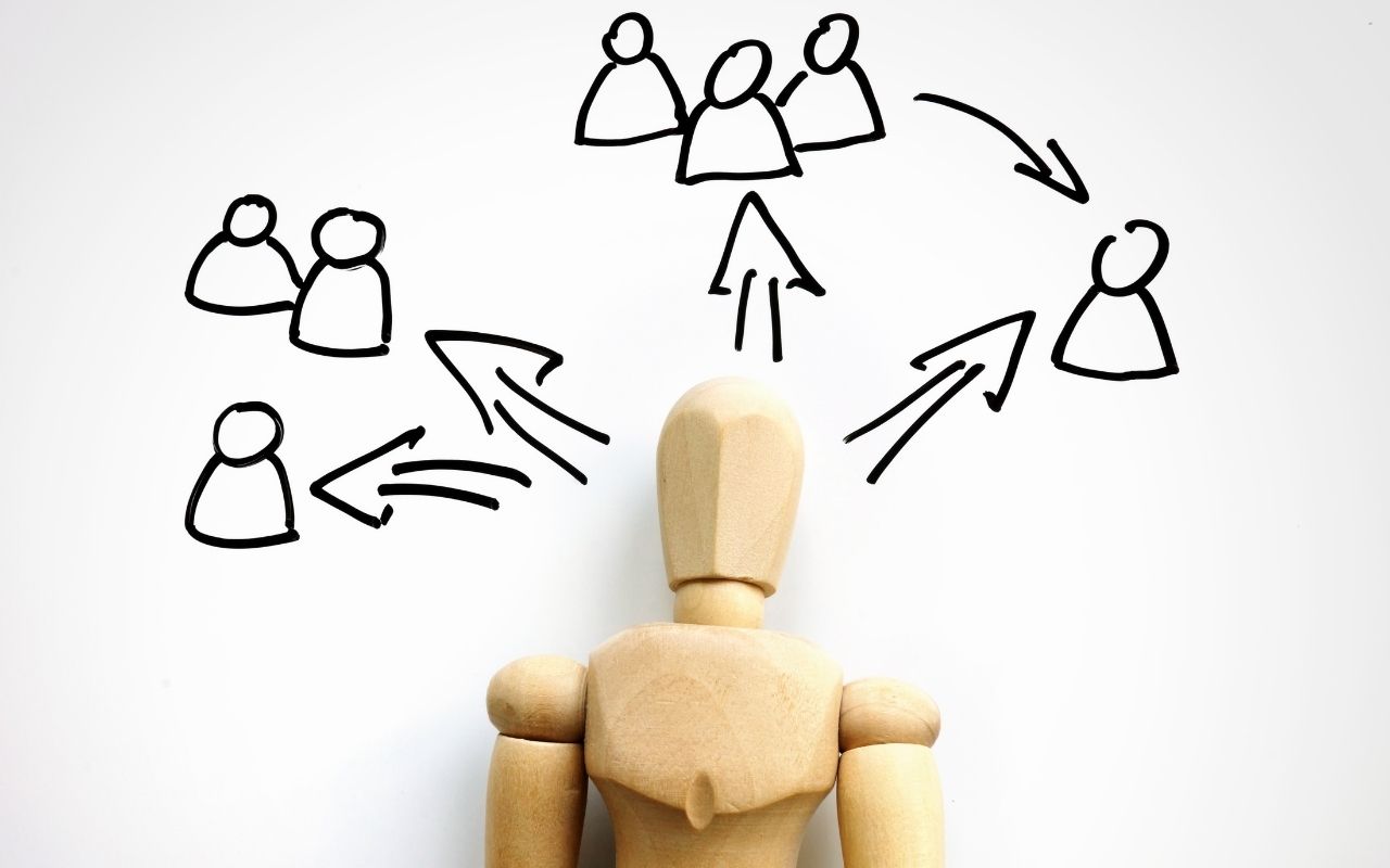 A humanlike figurine over a piece of paper with a drawing of a few groups of people forming from it.